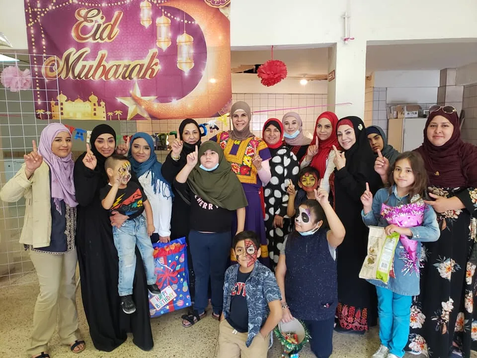Women and children celebrating Eid together in front of an Eid Mubarak banner