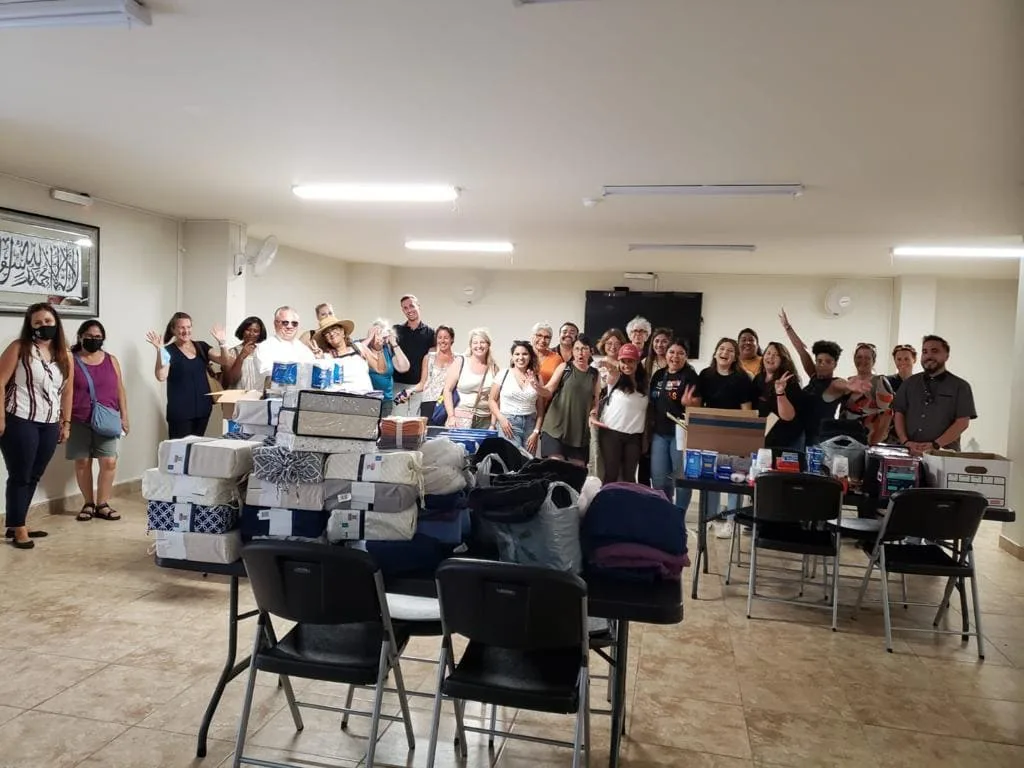 Volunteers and community members celebrating beside tables of donated bedding and supplies
