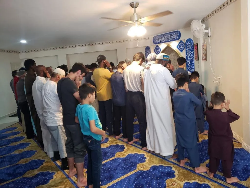 Men and boys standing together in congregational prayer in the shelter's prayer hall