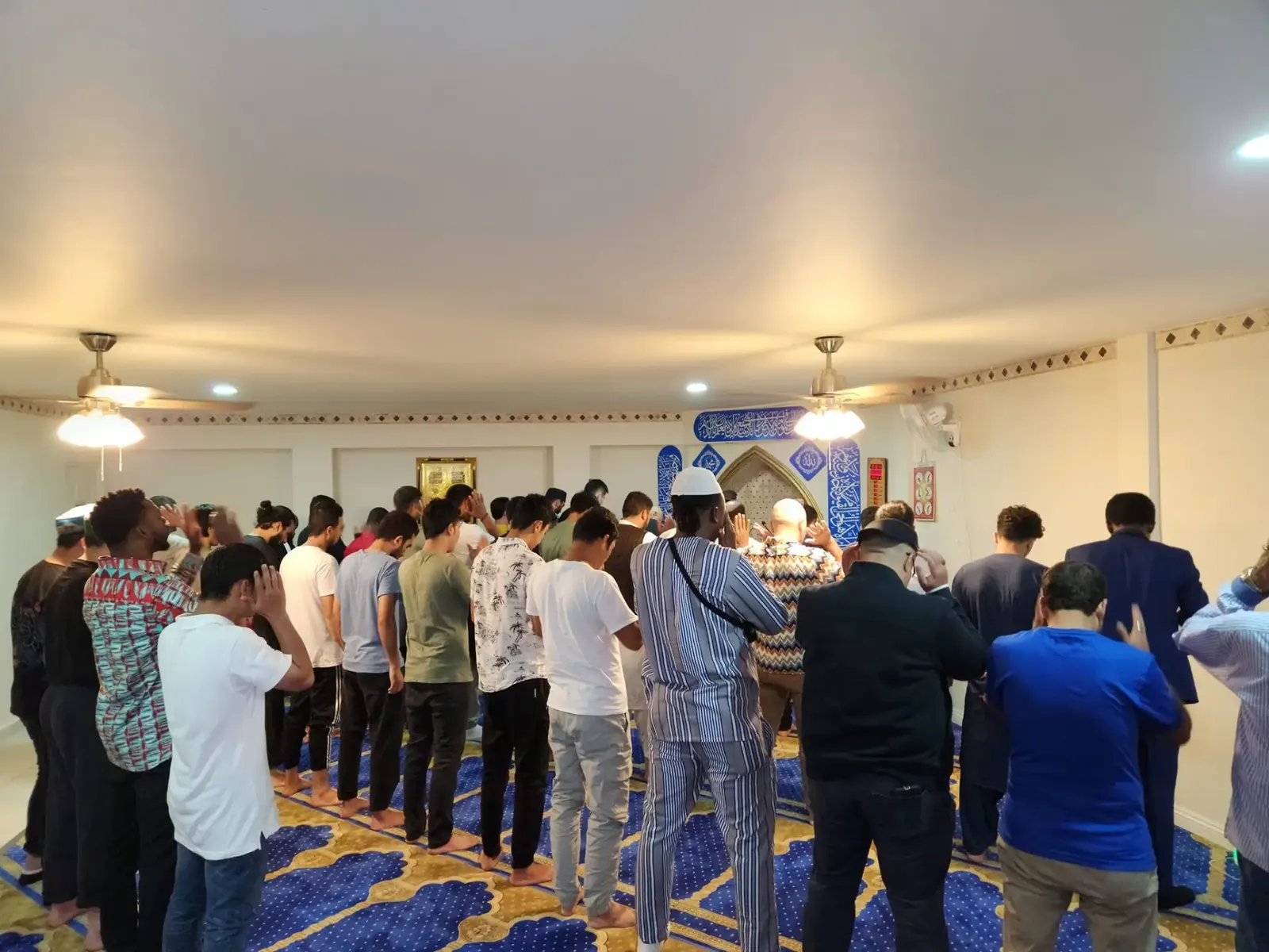 Worshippers standing together in congregational prayer in the prayer hall of an ALMA shelter